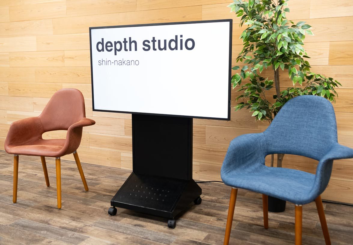 テレビ台つきの50インチモニター。画面に「depth studio shin-nakano」と表示され、両側に椅子が置かれている